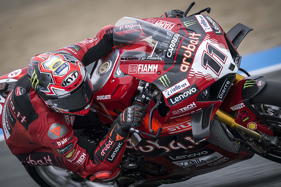 Nicolò Bulega cornering during a race of the 2024 Superbike Championship, riding his Ducati Panigale V4 R, with the Magneti Marelli Checkstar logo visible on his helmet.