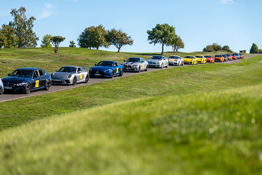 Line of sports cars with Magneti Marelli Parts & Services logo on an asphalt road surrounded by greenery during an incentive event in Prague for Italian partners.